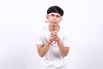 Asian young boy with red white ribbon for celebrating Indonesia independence day standing while making pleading gesture