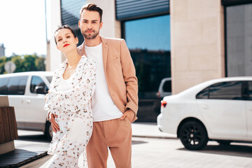 Wall Mural - Beautiful fashion woman and her handsome elegant boyfriend in beige suit. Sexy brunette model in summer clothes. Fashionable smiling couple posing in street Europe. Brutal man and female outdoors