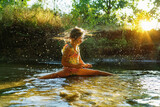 Fototapeta Lawenda -  little girl playing in the river. A girl with blond hair in a sunbeam surrounded by thousands of small drops.