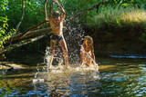 Fototapeta Lawenda - children playing in the river. A girl and boy raises her hands up in the water and splashes water drops