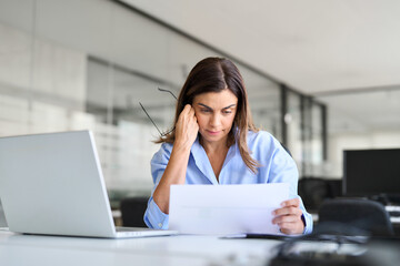 busy professional mature business woman reading bad news in document at work. worried serious middle