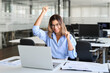 Happy excited professional middle aged business woman employee, executive or entrepreneur looking at laptop computer feeling joy celebrating victory corporate success sitting at work desk in office.