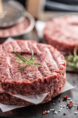 Wall Mural - Fresh raw ground beef patties with rosemary salt and pepper made in a meat form on a cutting board