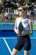 © Mat Hayward - Female pickleball player wearing black and white sports shirt and sunglasses holding ball and paddle while standing outside during a match on a blue court.