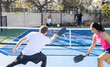 © Mat Hayward - Two on two doubles pickleball game on an outdoor court. Four players are athletic and competitive hitting the ball over the next with their paddle.