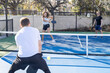 © Mat Hayward - Woman hits pickleball back to a man over the net on an outdoor court.