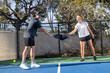© Mat Hayward - Co-Ed pickleball team playing a game together outside. The man and woman are athletic and working well as a team in the popular sport. They are tapping paddles like a high five.