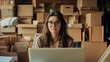 © Nemanja - Beautiful young businesswoman working on laptop notebook, smiling and sitting surrounded by cardboard boxes ready for shipping. Internet online store, order distribution work