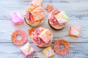 Wall Mural - Pastel colored pink cupcakes with chocolate, donuts and rainbow marshmallow