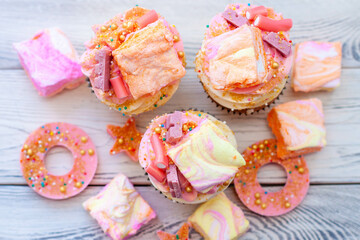 Wall Mural - Pastel colored pink cupcakes with chocolate, donuts and rainbow marshmallow