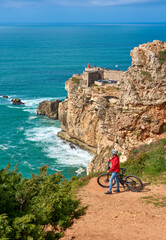 Wall Mural - nice senior woman riding her electric mountain bike on the rocky cliffs of Nazare at the western atlantic coast of Portugal