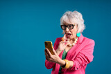 Fototapeta Młodzieżowe - Surprised Senior Woman Using Smartphone in Pink Blazer