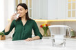 Woman drinking water in kitchen, focus on filter jug