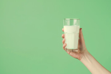 hand holding glass with milk on green background