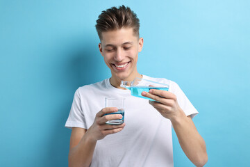 Canvas Print - Young man using mouthwash on light blue background