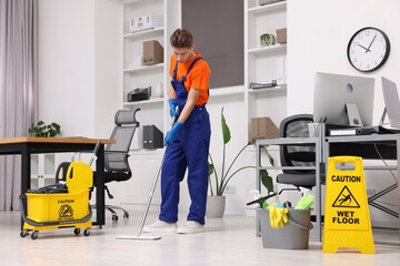 Wall Mural - Cleaning service worker washing floor with mop. Bucket with supplies and wet floor sign in office