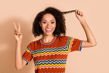 Sticker - Portrait of cheerful girl with wavy hairstyle dressed ornament t-shirt showing v-sign demonstrate curl isolated on pastel color background