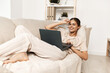 © SHOTPRIME STUDIO - Smiling woman working on laptop in cozy home office, surrounded by modern technology and online connection.