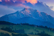 mountain sunset in the spring with Ceahlau peak in snow and green meadow on countryside of Romania Carpathians.