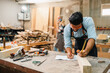 © chokniti - Carpenter working with electric planer on wooden plank in workshop. Craftsman makes own successful small business, man using tool in carpenter's shop to making a furniture from wood