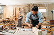 © chokniti - Carpenter working with electric planer on wooden plank in workshop. Craftsman makes own successful small business, man using tool in carpenter's shop to making a furniture from wood