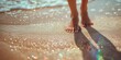 Women's bare feet on the sand, the grains of sand shine colorfully in the light from the sunny daylight on the sea beach