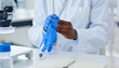 © peopleimages.com - Gloves, hand and book in lab and medicine, innovation and future of healthcare with science and research. Workplace, safety and expert of pharmaceutical, working and notebook for discovery of cure