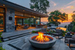 A photo of a large, round fire bowl placed on an outdoor patio with modern architecture and glass windows overlooking the sunset in California's backyard landscape design. Created with Ai