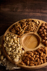 Wall Mural - Cashews, almonds, hazelnuts and walnuts are laid out on a wooden menagerie. Top view of a round wooden plate with different nuts standing on burlap on the table. 