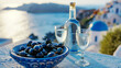 © Myroslava - Greek aniseed drink Ouzo in a glass bottle with two shot glasses and Greek olives on a traditional ceramic dish, with a landscape of the Mediterranean coastline in the background