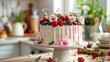 Beautifully decorated cake with fresh berries and flowers on stand in home kitchen
