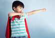 Boy, studio and superhero cape with happy for child development with playing, confidence and youth for fantasy. Blue background, cosplay and costume with brave or strong with ready to protect freedom