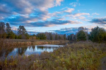 Wall Mural - Autumn landscape with riverbank at sunset. Wonderful nature, beautiful natural background. Sky with clouds is reflected in the water.