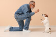 Senior man playing with cute dog against beige wall