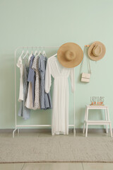 Wall Mural - Rack of trendy clothes and hats near white wall