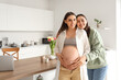 © Pixel-Shot - Young lesbian woman hugging her pregnant wife in kitchen