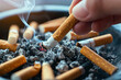 close-up or macro of cigarettes in an ashtray, hand holding a cigarette end 