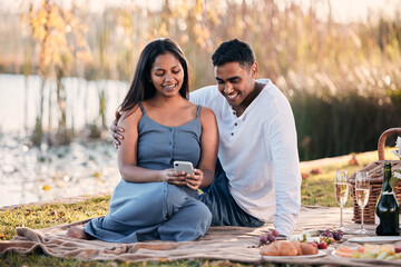 Poster - Couple, picnic and phone for social media in outdoors, nature and relax on grass for bonding. People, lake and app for funny joke or online humor on vacation, travel and browse tech on park date