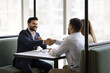 © fizkes - Positive confident young Indian lawyer in formal suit giving legal consultation to couple of customers, meeting with clients at cafe table, shaking hands with husband and wife, laughing