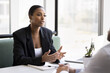 © fizkes - Serious beautiful African American consultant woman talking to customers at business meeting, sitting at cafe table, speaking. Real estate agent, bank broker, financial advisor giving consultation