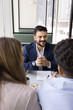 © fizkes - Cheerful young Indian consultant man in formal suit meeting with couple of young husband and wife, talking to clients, customers, smiling, sitting at coworking cafe table