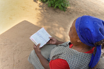 village Christian old african woman ,reading religious holly bible book, casual dressed with blue headscarf
