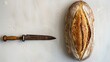   A loaf of bread sits next to a knife on the table One slice of bread is placed on the table as well