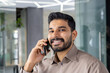 A cheerful professional man is engaged in a friendly phone conversation, smiling in a modern office setting. This image captures a moment of positive workplace interaction.