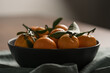 Small organic tangerines with leaves in ceramic bowl on wood table