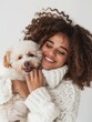 Smiling woman in a knitted sweater cuddles a fluffy dog, sharing a moment of joy and companionship.