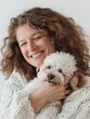 A smiling woman with curly hair lovingly holding a small white dog, expressing affection and companionship.