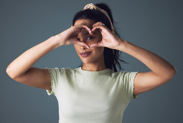 Girl, fashion and eye with heart hand in studio on grey background in casual, style and gen z. Portrait, smile and cool with emoji or love sign and symbol for appreciation, support and positive