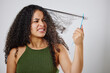 Messy hair, tangle and frustrated woman with comb in studio for knot, stress and problem on grey background. Curly, haircare and model annoyed with brushing fail, damage or styling hairloss results