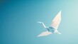A single origami crane in flight against a clear blue sky. 
